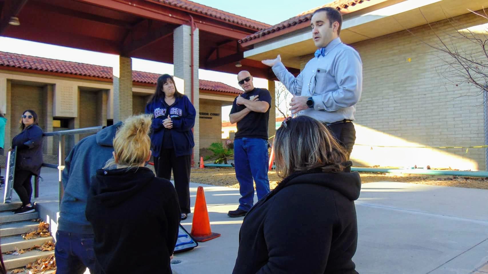 Brett Haddoak gesturing as he speaks to a group of volunteers gathered outside a school building.